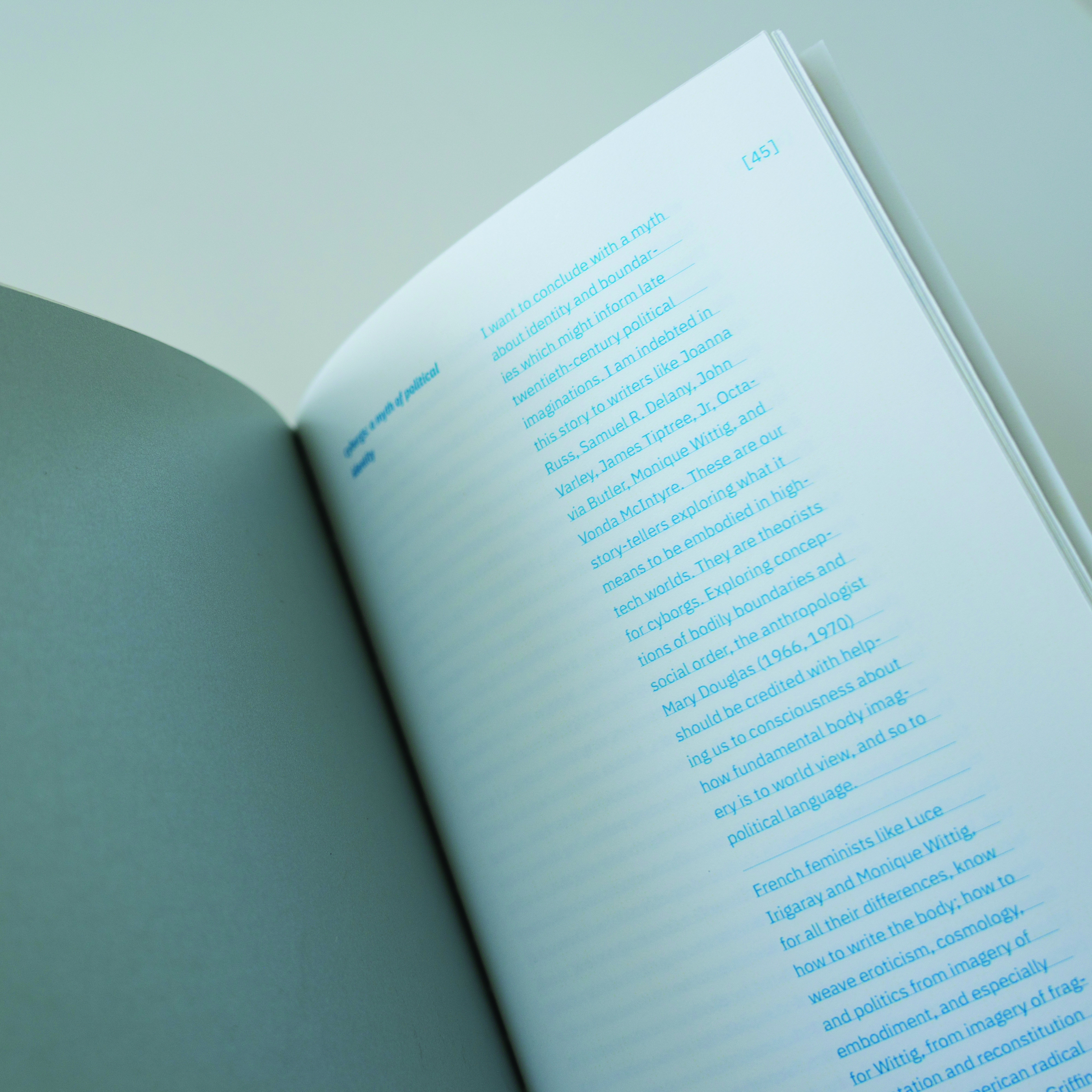 An opened book showing a white page with narrow columns of blue text and a diffused metallic page opposite it.